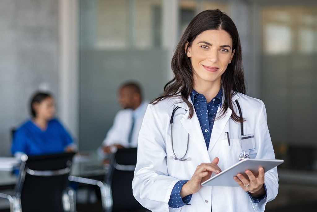Un médecin en blouse blanche vérifie un comprimé et sourit.